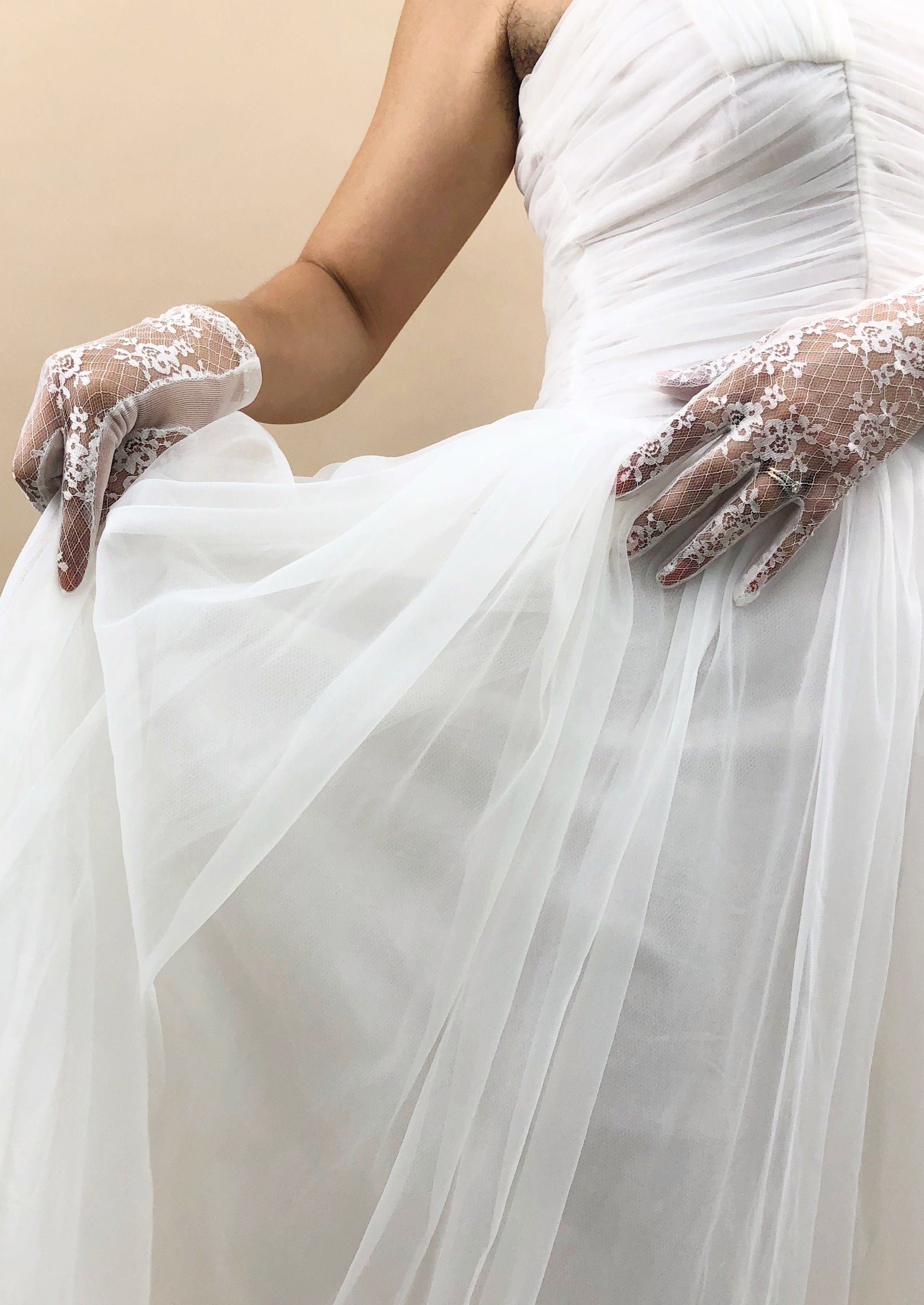 hands with gloves on, holding chiffon dress up